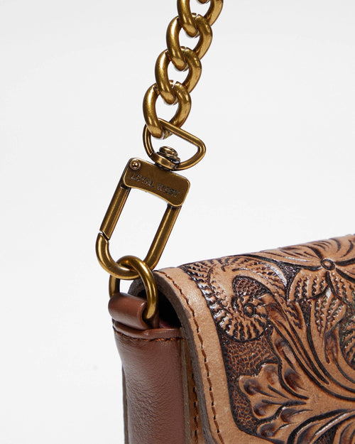 Close-up of a brown leather handbag with intricate floral tooled design and gold chain strap.
