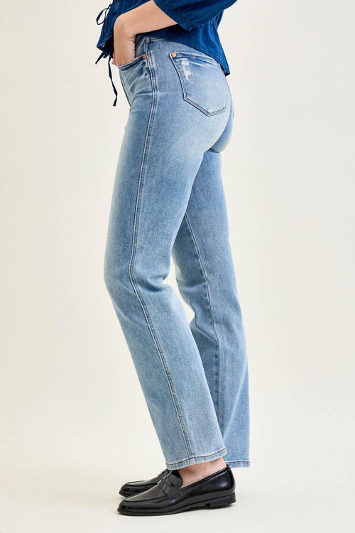 Person wearing light blue jeans and black shoes on a plain background