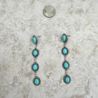 Turquoise and silver earrings on a textured surface with a coin for scale.