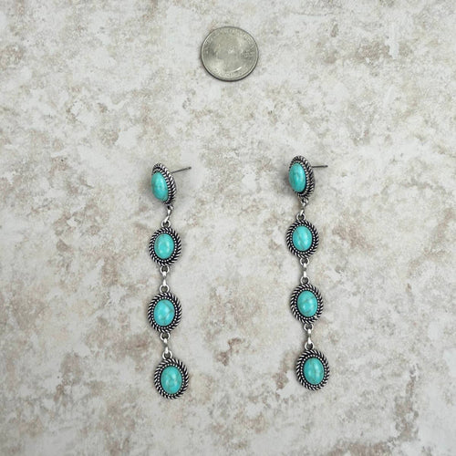 Turquoise and silver earrings on a textured surface with a coin for scale.