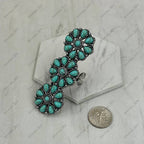 Turquoise and silver brooch on a gray background with a coin for scale.
