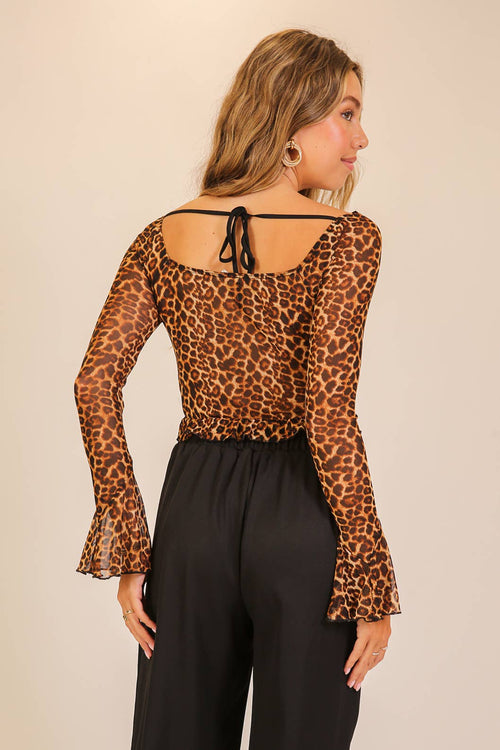 Woman wearing a leopard print top with long sleeves and black pants on a beige background