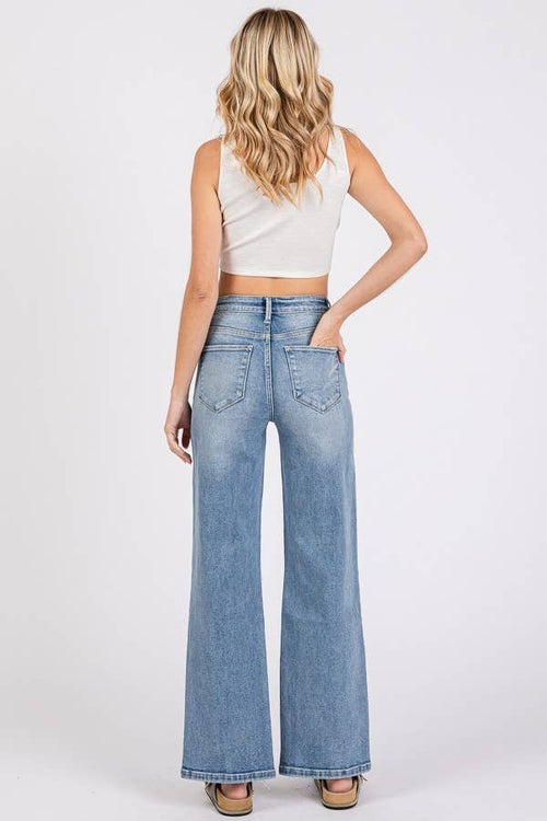 Woman wearing light blue flared jeans and a white top on a white background