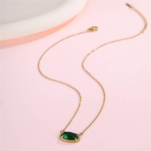 Gold necklace with a green gemstone pendant on a pink background