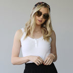 Woman wearing a white top and black skirt with sunglasses and a floral headband.