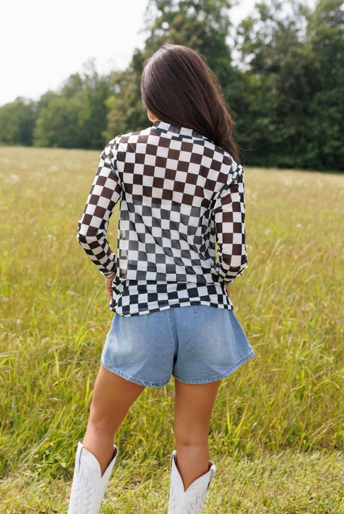 Person wearing a checkered shirt and denim shorts standing in a field.