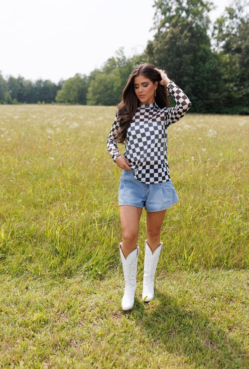 Woman in a checkered shirt and denim shorts standing in a field