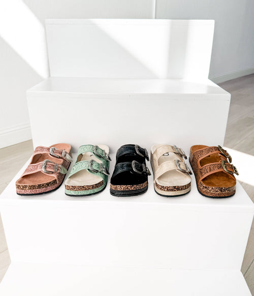 Five pairs of sandals on a white surface with a white box in the background