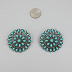 Pair of turquoise earrings on a white surface with a coin for scale.