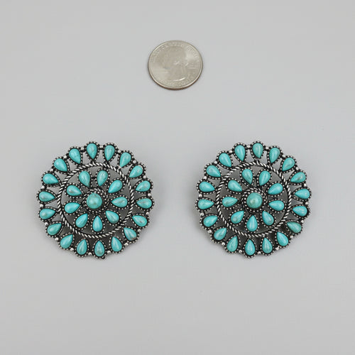 Pair of turquoise earrings on a white surface with a coin for scale.