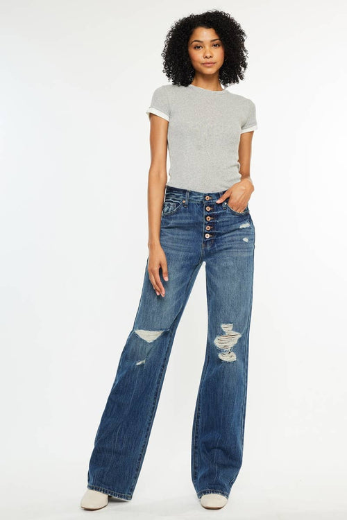 Woman wearing a gray t-shirt and blue jeans with button details on a white background