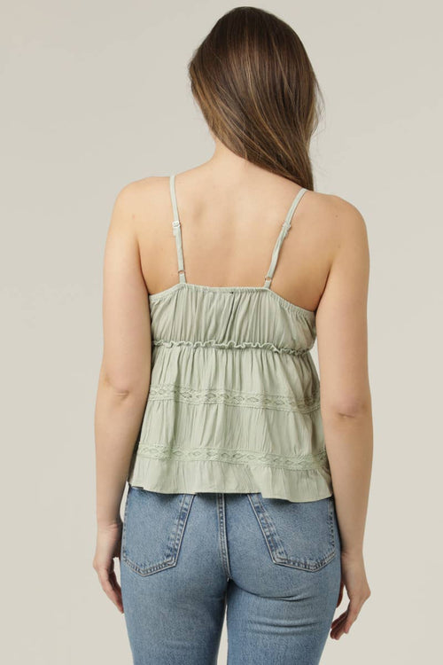 Woman wearing a light green tank top and blue jeans against a neutral background