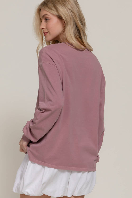 A woman shown from the back wearing a dusty rose long-sleeve crewneck sweatshirt and a white skirt, set against a plain light beige studio background.