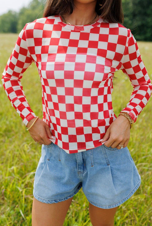Person wearing a red and white checkered shirt with denim shorts in a grassy field