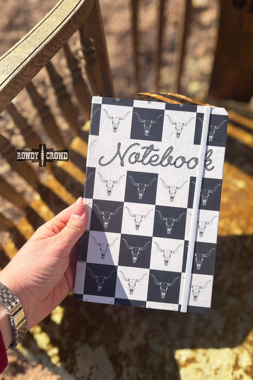 Notebook with checkered pattern and bull head design held by a hand outdoors.