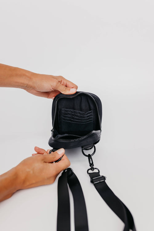 Person holding a black leather pouch with a strap on a light gray background