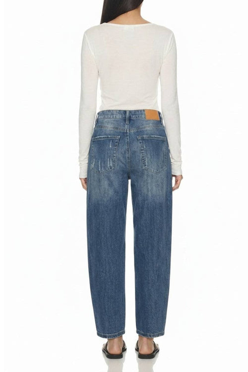 A model shown from the back wearing a white long-sleeve top and blue wide-leg jeans with a brown leather patch on the back waistband, set against a plain white background.