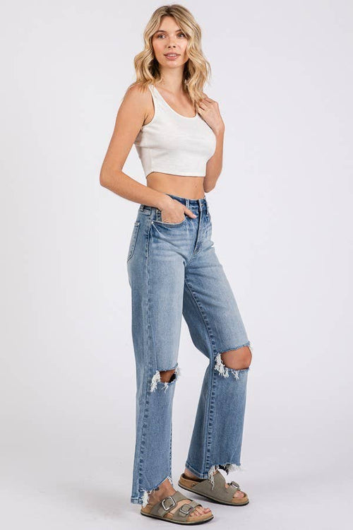 Woman wearing a white crop top and distressed blue jeans on a white background