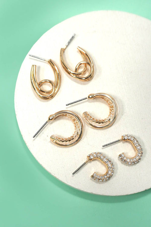 Set of gold hoop earrings on a white circular stand against a green background