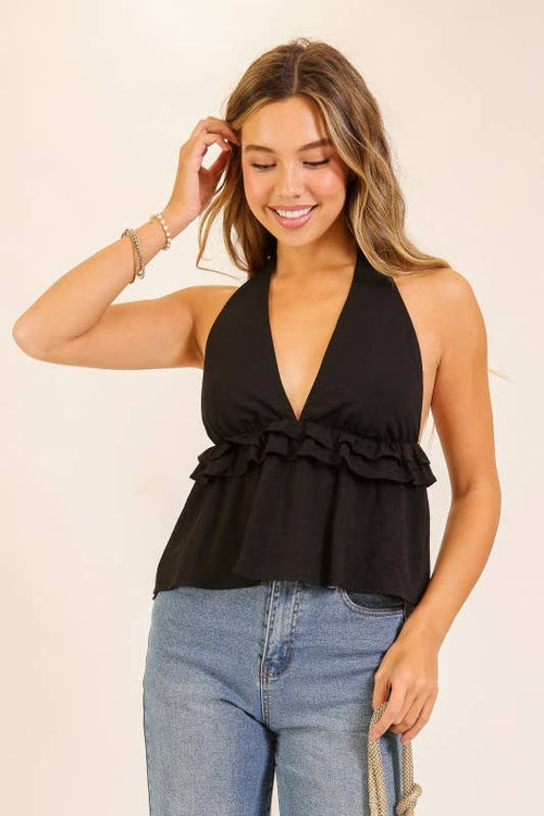 Woman wearing a black halter top with ruffles and blue jeans on a beige background