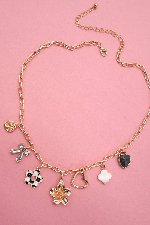Gold necklace with various charms on a pink background