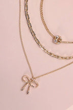 Gold chain necklaces with bow charm on a pink background