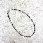 Silver beaded necklace on a textured beige surface