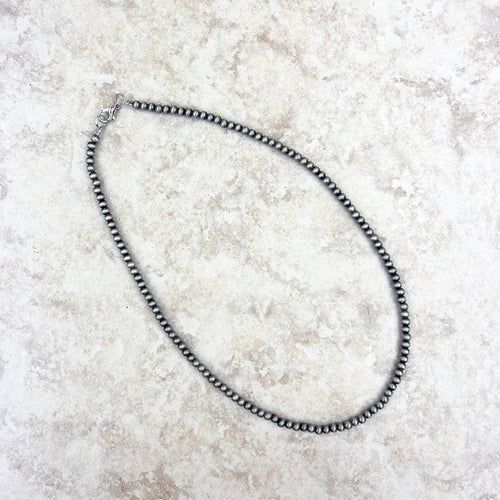 Silver beaded necklace on a textured beige surface
