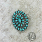 Turquoise stone belt buckle on a textured surface with a coin for scale.