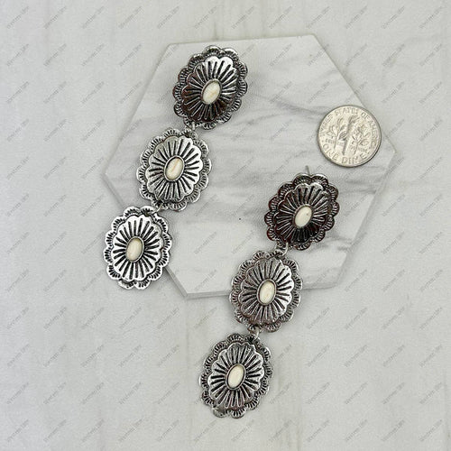 Silver concho-style earrings on a textured white surface with a coin for scale.