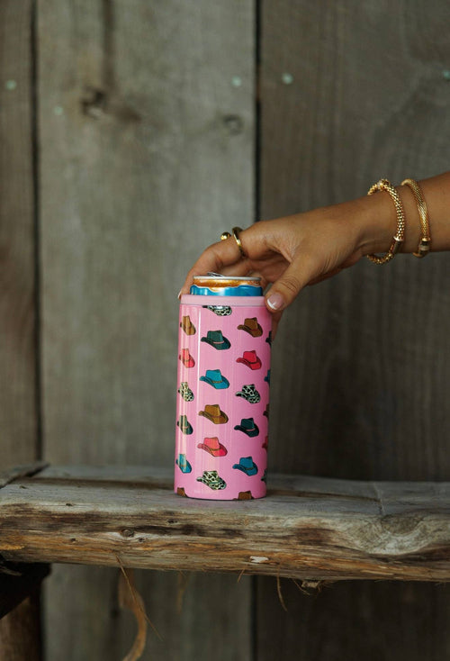Hand holding a pink can with colorful designs against a wooden background
