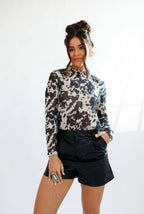 Woman wearing a patterned long-sleeve top and black shorts against a white background