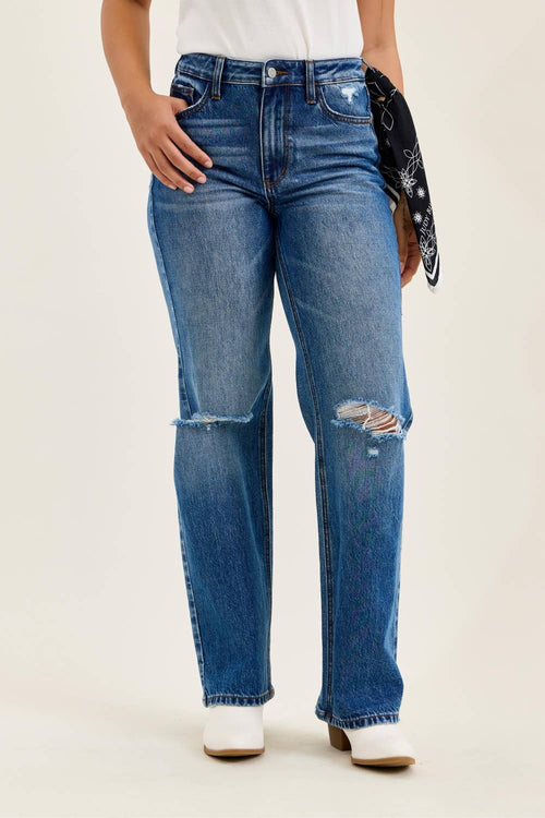 Person wearing blue jeans with slight distressing on a plain background