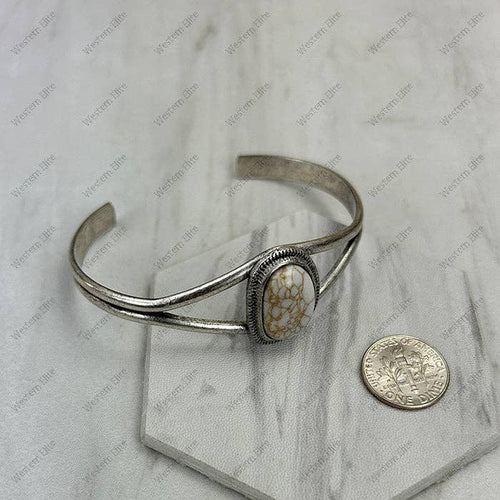 Silver bracelet with a stone inlay next to a coin on a marble surface
