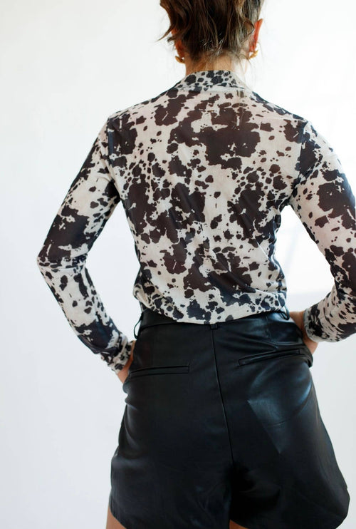 Person wearing a patterned blouse and black pants against a white background
