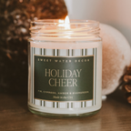 Candle labeled 'Holiday Cheer' from Sweet Water Decor on a wooden surface with decorative elements.