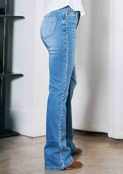 Person wearing blue jeans with decorative buttons in a minimal indoor setting.