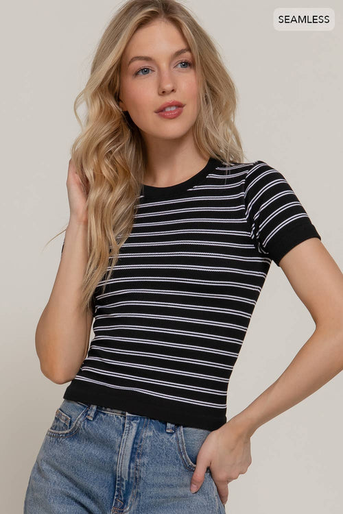 Woman wearing a black and white striped shirt with blue jeans on a plain background