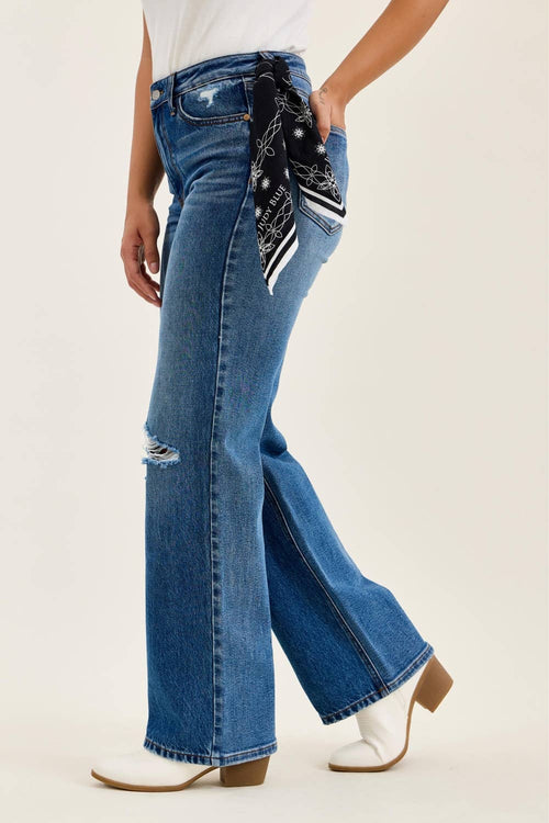 Person wearing blue jeans with a patterned bandana, white shirt, and white shoes on a beige background