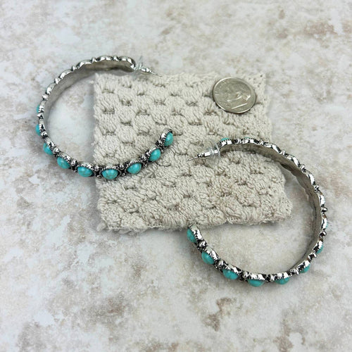 Two silver hoop earrings with turquoise beads on a textured surface.