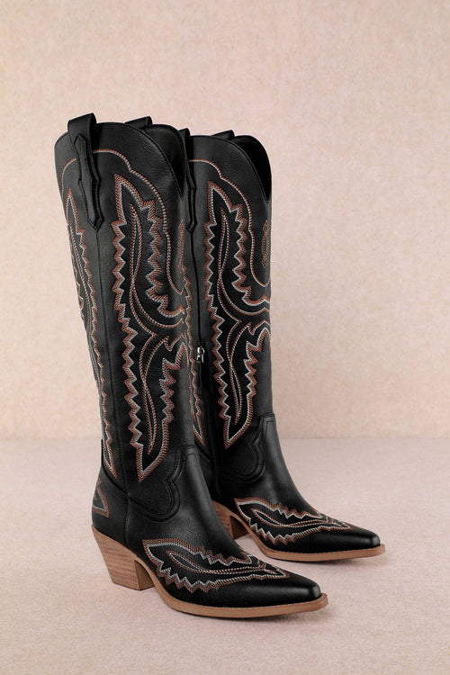 Pair of black cowboy boots with intricate designs on a beige background