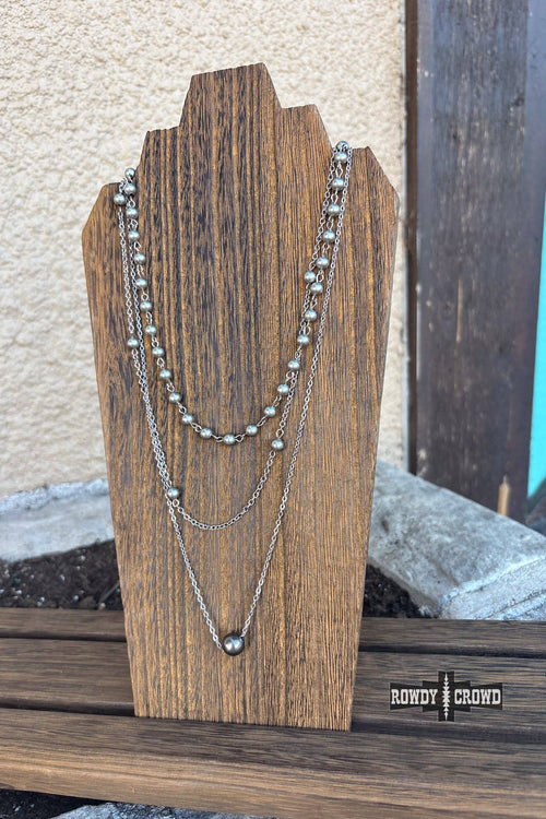 Three silver necklaces on a wooden stand with a blurred background