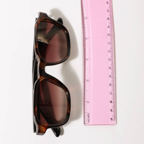 Sunglasses next to a pink ruler on a white background