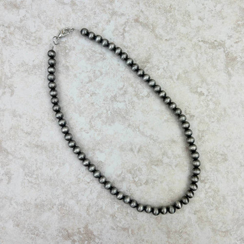 Black pearl necklace on a textured beige surface