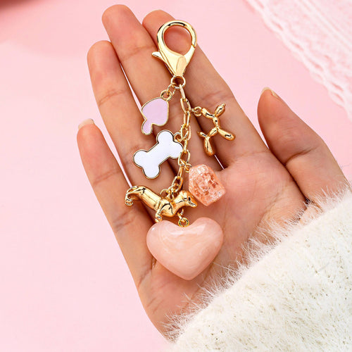 Hand holding a keychain with various charms against a pink background