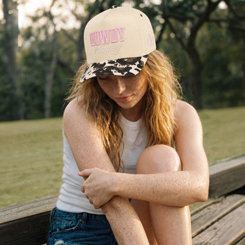 Woman sitting on a wooden bench outdoors wearing a cap with text.