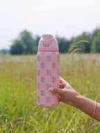 Hand holding a pink water bottle with text in a grassy field