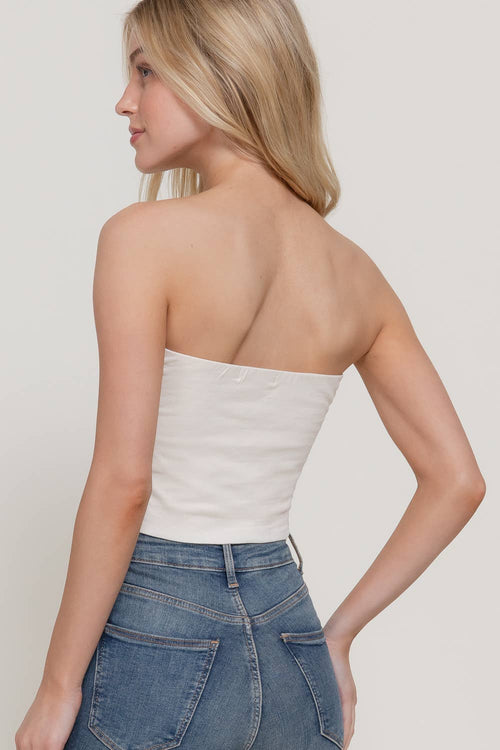 Woman wearing a white strapless top and blue jeans on a plain background