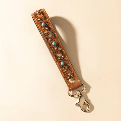 Brown leather strap with embossed designs and turquoise beads on a beige background