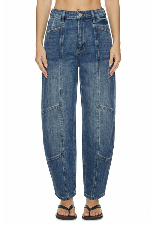 A model wearing a pair of high-waisted, wide-leg blue denim jeans with distinctive diagonal seam details on the legs, paired with black flip-flop sandals against a plain white background.